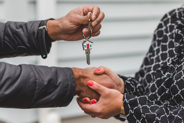 A close-up photo of a real estate agent handing keys with a keychain in the shape of a house to a buyer